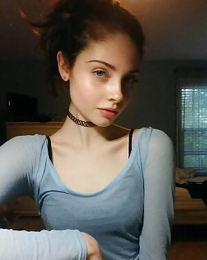 a woman with a blue shirt and a black choker on her neck and a bed in the background